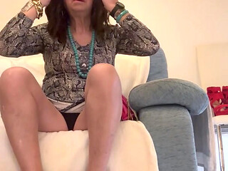 Beautiful Spanish trans woman poses sensually on the living room sofa in a pretty dress and colorful high heels