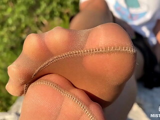Mistress in tan tights teases you with her cute feet outdoors