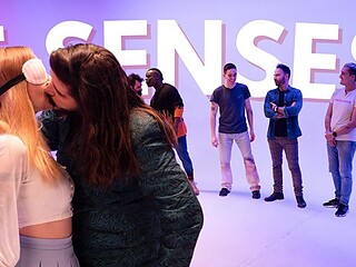 Blindfolded blonde in white lace-up crop top kisses long-haired man in green jacket
