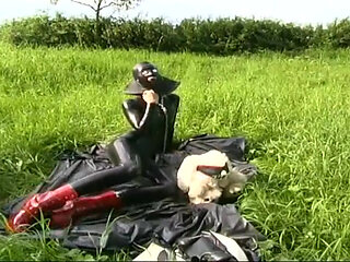 Fetish slave in latex walks and sucks a dildo on the grass